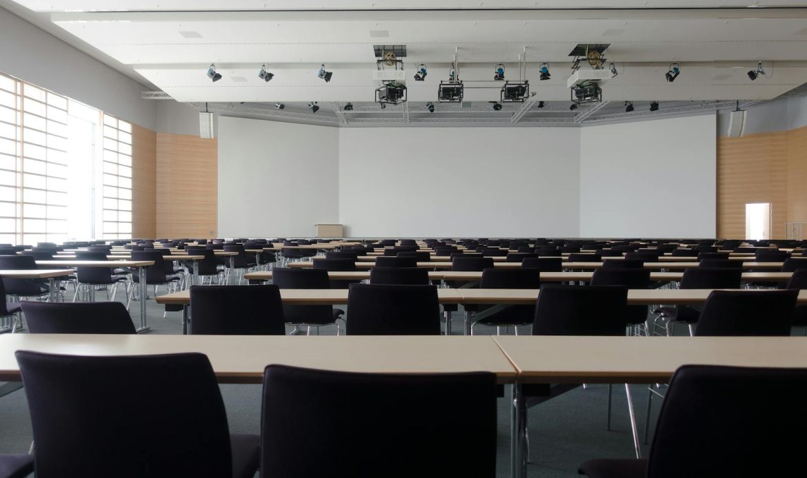 Spacious contemporary conference room with rows of tables and chairs, ready for meetings.