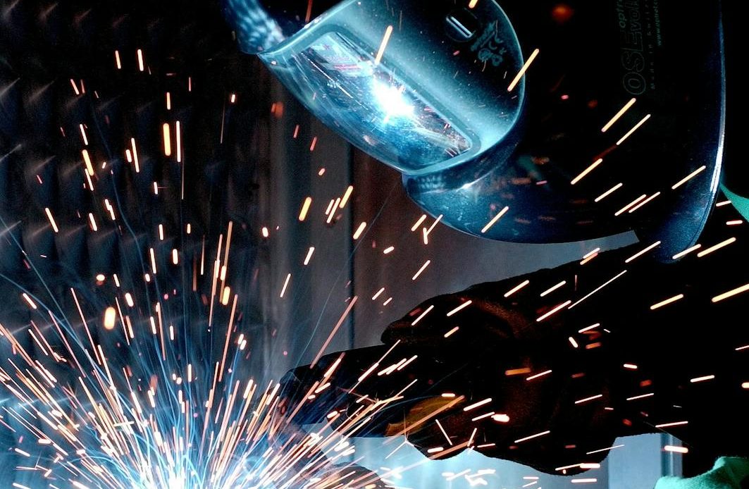 A focused welder works with metal in an industrial setting, creating vibrant sparks.