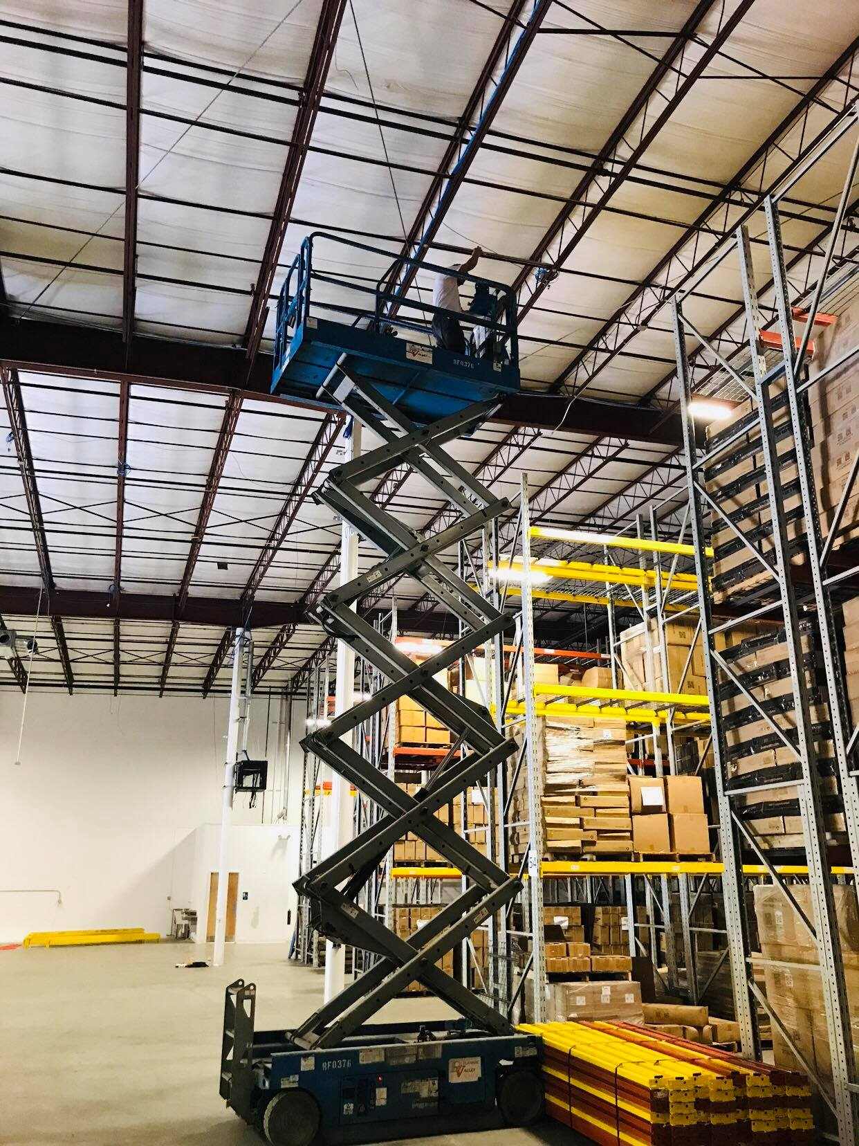 Scissor lift work installing network equipment above warehouse racking